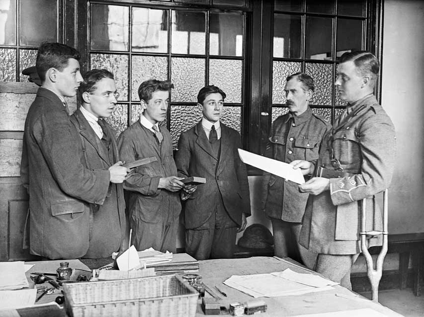 As an army officer reads out the oath, four young men hold Bibles and confirm their allegiance at a recruitment office. Note that the Bibles are shared. British recruitment officer Coulson Kernahan recalled farcical instances of twelve or more recruits who would ‘hold on with their right hand for dear life to one persecuted Testament while being attested in batches’. (IWM)